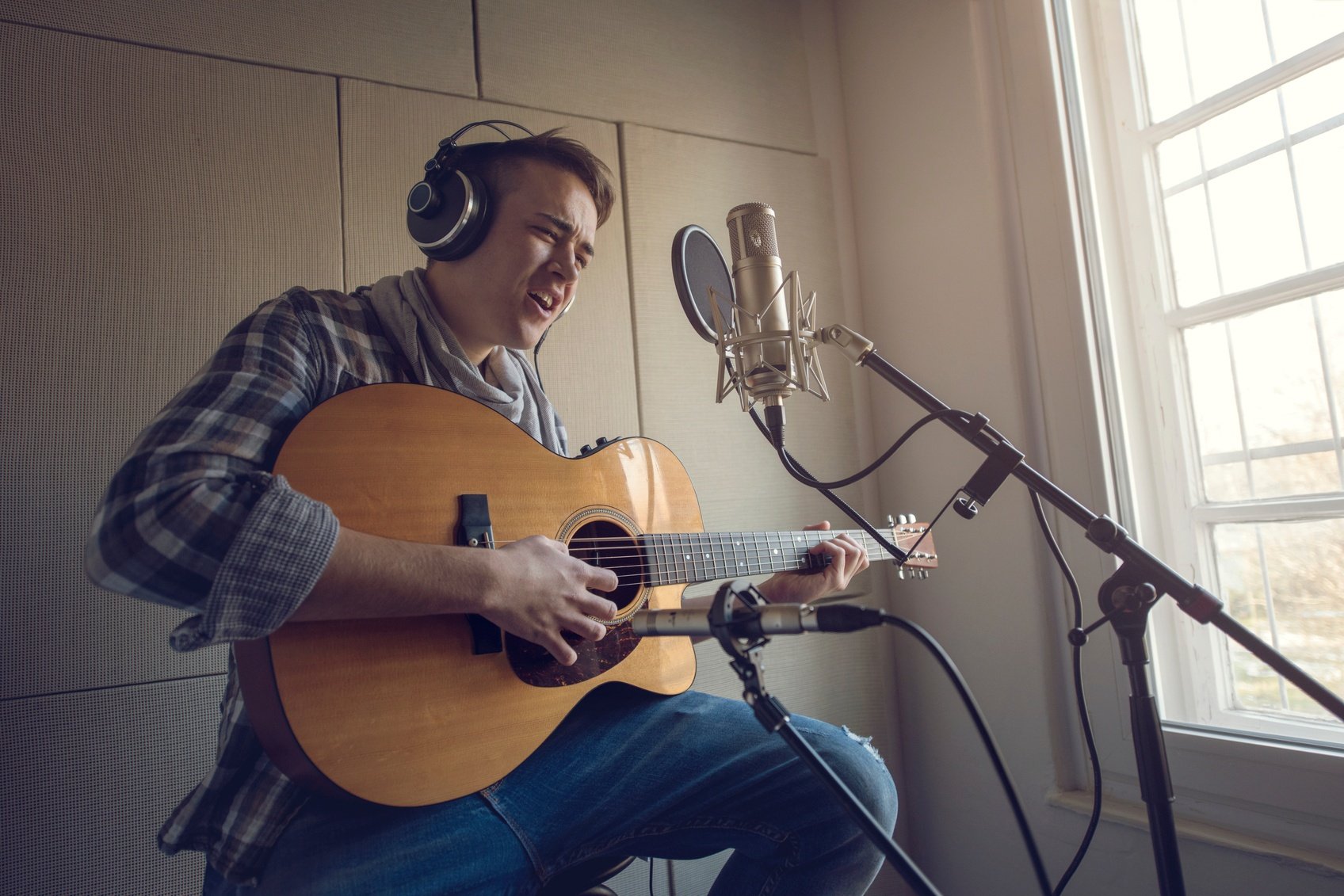 Young-man-playing-acoustic-guitar-and-singing-in-recording-studio-000087459773_Medium